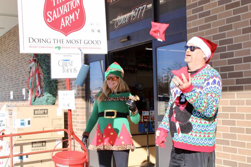 Larry Stevens, 56, engages in some attention-getting juggling while Jen Gottschalk, 55, serves as a bell-ringer do some music being placed on a wireless speaker as they start their shift at The Salvation Army kettle in front of Ace Hardware in Dixon. The pair were representing Crest Foods, relieving the earlier bell ringers, Jackie Fransen and Henry Fransen, age 8.