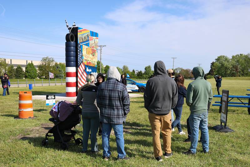 A small crowd hangs out at the unveiling of the new Route 66 sculpture along South Chicago Street at the Route 66 Raceway on Tuesday, May 12, 2026 in Joliet.