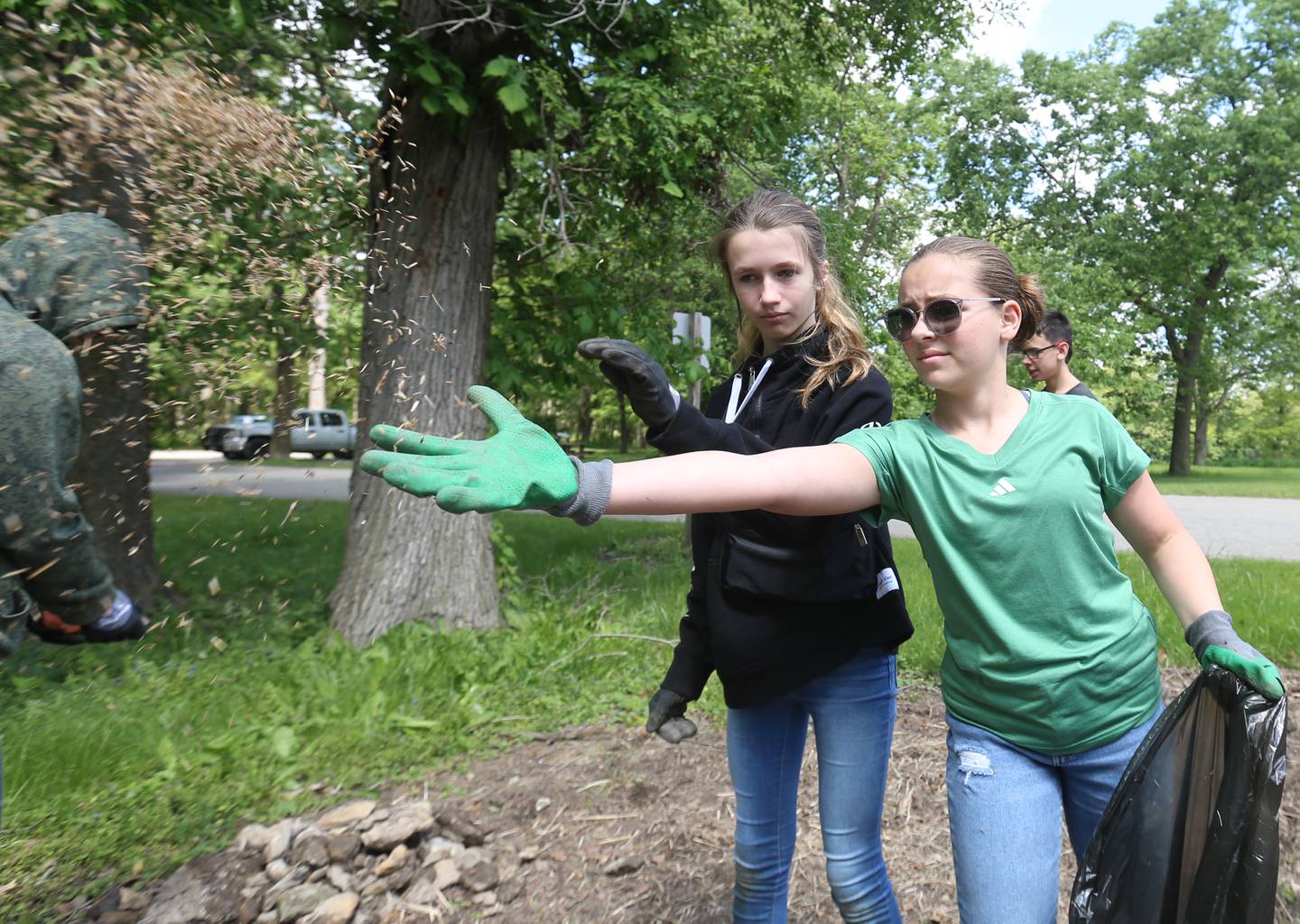 Milton Pope students Alexandra Aubry and Jillian Lambert spread pollinator seed on Friday, May 23, 2025 near entrance to Illini State Park in Marseilles. Milton Pope students volunteered their time planting seed, pulling up rocks, spreading mulch and helping with other tasks.