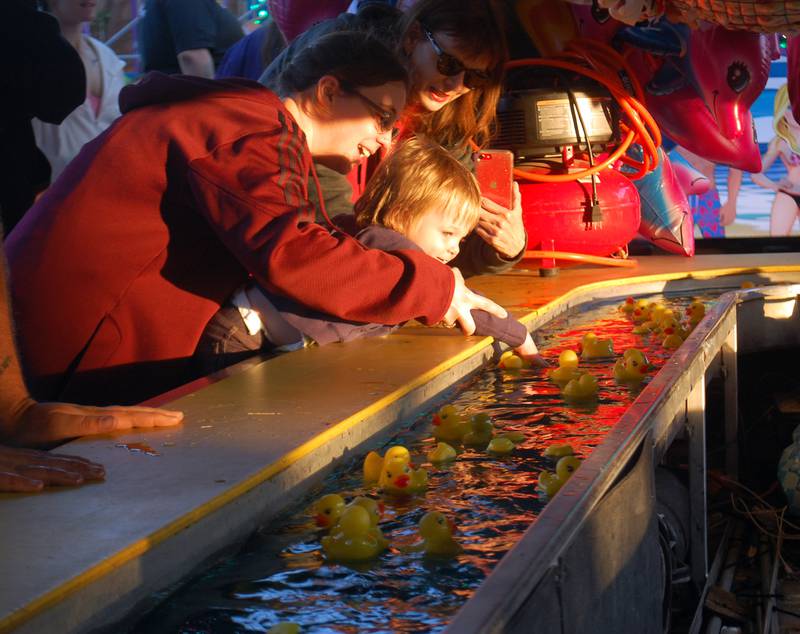 Axel Hersheway reaches for a rubber duck with help from his family during a carnival game at Streator Park Fest on Friday, May 26, 2023.