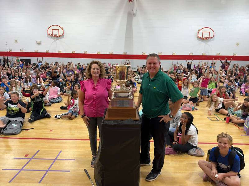 Bradley West Elementary School assistant principal Jeff Voss, right, and his wife, Jennifer, stand in front of Bradley West students with the Kankakee County Amateur Men's Golf Tournament trophy he won earlier this month.