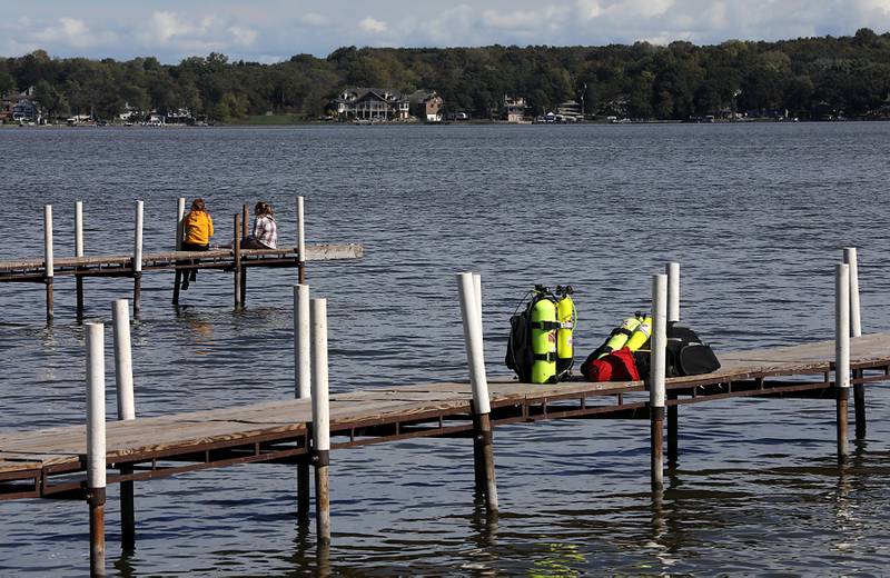 Two women sit on the end of a dock as divers from the Antioch Fire Protection District and a sonar team from the Illinois Department of Natural Resources continue searching Tuesday, Oct. 7, 2025, on Fox Lake near Antioch for a man thrown from a boat he was test driving Monday night.