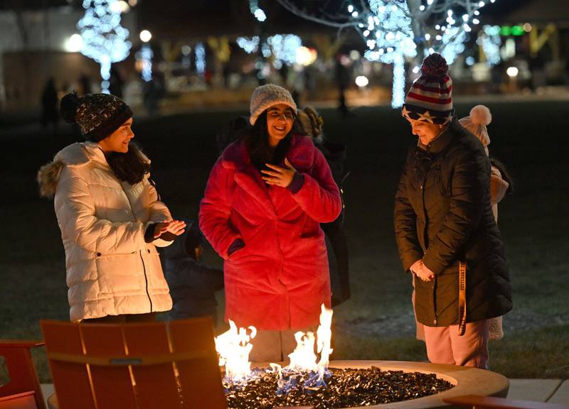 Samantha Sadulla, 12, along with Liona Gusho and mother, Bruna Sadulla, all of Bourbonnais, share warmth from one of the new fire pits on Thursday during the inaugural tree lighting at The Grove in Bourbonnais.