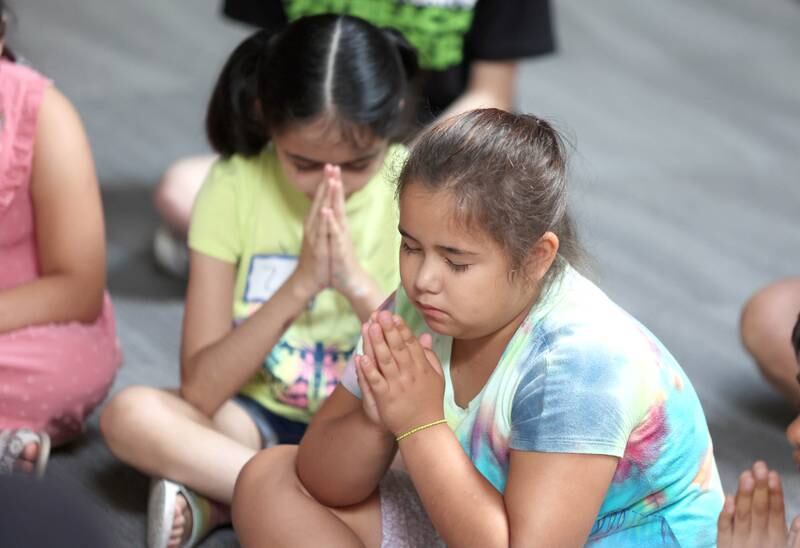 Aylin Salazar, (right) 7, from DeKalb, along with other participants fold their hands as an opening prayer is said Monday, July 11, 2022, at the beginning of a session of Summer Reading Vacation put on by Neighbors' House in DeKalb in conjunction with the DeKalb County Farm Bureau. Christ Community Church is hosting the camp this week in their outreach center on North 6th Street in DeKalb.