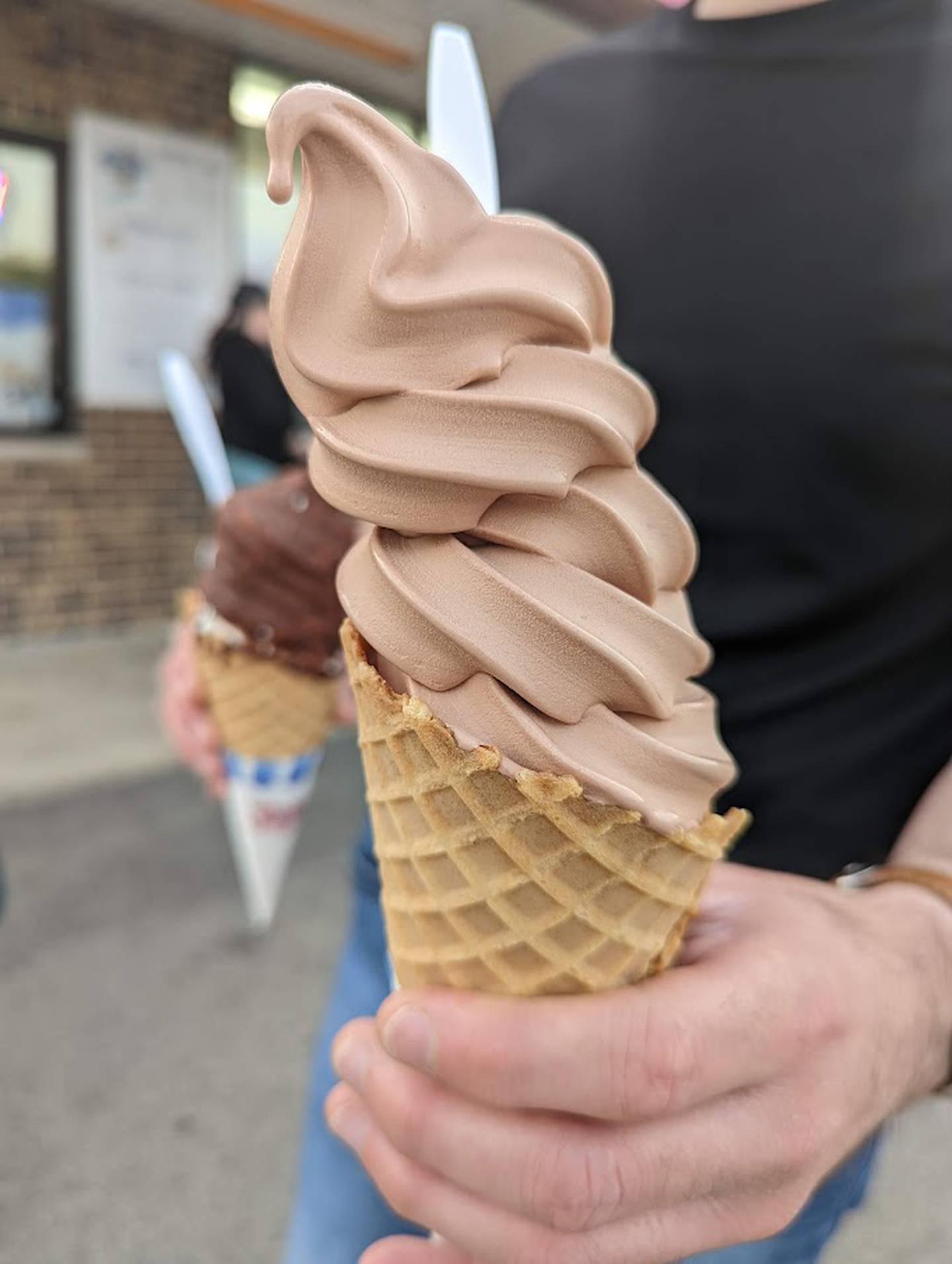 In the foreground is the chocolate swirl ice cream cone as served at Minooka Creamery. The vanilla swirl ice cream with a chocolate topping is in the background. Both were served on waffle cones.