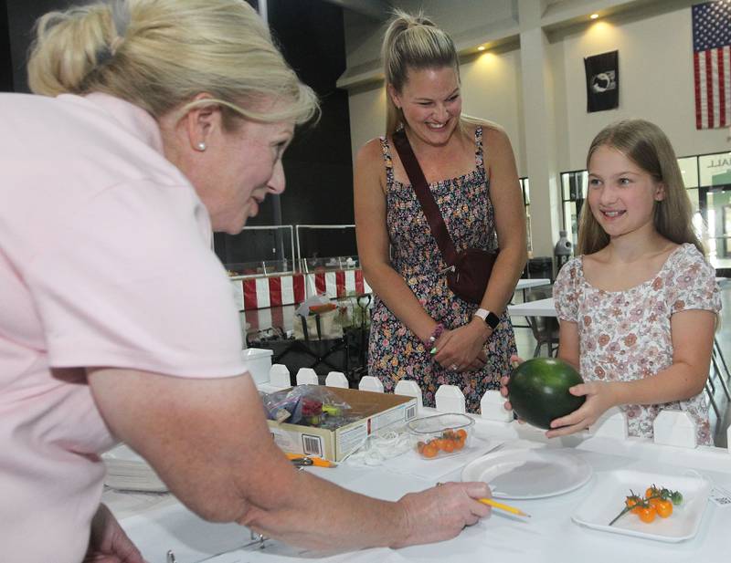 Robbie Roberts, of Grayslake, a volunteer, talks with Olivia Kottmeyer, 11, of Grayslake about the watermelon and cherry tomatoes she was entering in the fruit category under Garden while she was checking-in at the Expo Hall before the start of the Lake County Fair on Tuesday, July 25th at the Lake County Fairgrounds in Grayslake. Olivia's mother, Kelli, was by her side.The fair runs from July 26th-30th.
Image by Candace H. Johnson for Shaw Local News Network