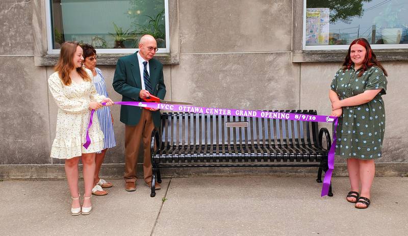 Illinois Valley Community College President Jerry Corcoran cuts the ribbon to the bench donated in his honor Wednesday, June 28, 2023, as his wife Katherine looks on. The ribbon held by his granddaughter’s Katie and Emma was the original 2010 ribbon used to open the IVCC Ottawa Center where the bench is located.