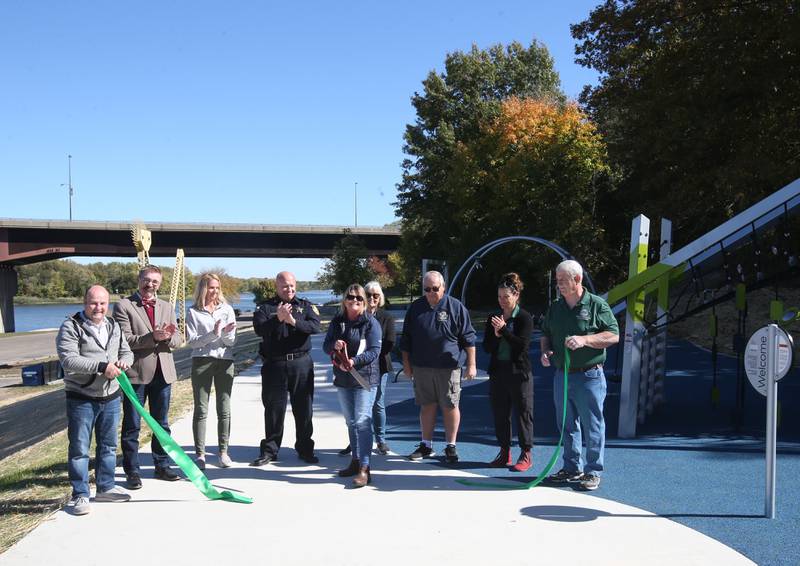 The City of Ottawa held a ribbon-cutting ceremony on Thursday, Oct. 17, 2024 at Allen Park in Ottawa. Commissioner Marla Pearson (center) cuts the ribbon on a 1.5 million dollar completion of a playground and other improvements to the park. The project was partially funded by a $506,000 IDNR Open Space Land Acquisition and Development grant. The new enhancements to Allen Park include accessible sidewalks leading to the upper plateau, featuring a modern playground and hillside play area with safe, poured-in-place surface for children of all abilities. The area also includes a shelter, bench swing with views of the Illinois River and a stone council ring for relaxation and community gatherings. 
A paved quarter-mile looped walking trail along the scenic banks of the Illinois River, two designated gaming areas, one with four bag toss stations and another with two chess-checkers tables and two ping-pong tables, all designed to promote social interaction and recreation. The sculptures will be repainted in the spring of 2025.