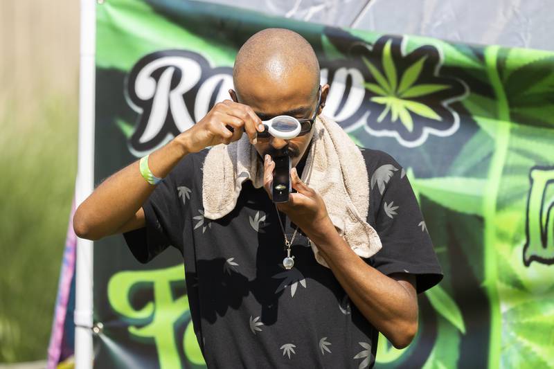 Using the power of the sun, Kaleb Harris uses a magnifying glass to light his pipe Friday, July 12, 2024 at Herbal Roots’ Cannafest at Elks Page Park.