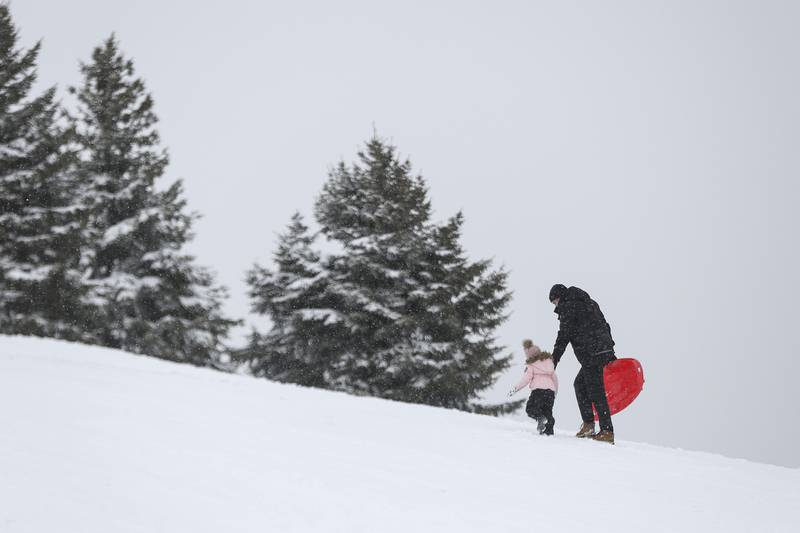 Travis Carpenter and his daughter Savannah make their way up the sledding hill for their first run of the day on Sunday, Jan. 31, 2021, at Cene's Four Seasons Park in Shorewood, Ill.  Nearly a foot of snow covered Will County overnight, resulting in fun for some and challenges for others.