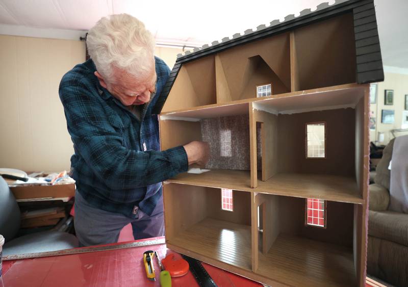 Sycamore resident Lee Newtson puts some wall paper in one of the rooms of a dollhouse Thursday, March 24, 2022, at his home in Sycamore. This dollhouse will be raffled off as a fundraiser to benefit Ukraine.