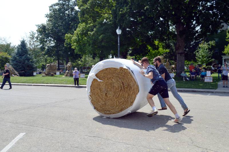 Keegan Shirley (left), of Dixon, and Jonathan Ulrich, of Beloit, Wisconsin, race to roll a 1,000 pound straw bale Saturday, Aug. 24, 2024, at StrawFest in downtown Mt. Morris. StrawFest was a part of the ninth annual U.S. National Straw Sculpting Competition.