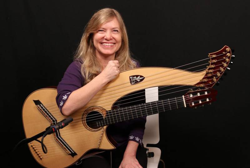 Guitarist Muriel Anderson, seated with her harp guitar, pauses and smiles between songs at a live show. She will appear Nov. 30 2024 in Downers Grove.