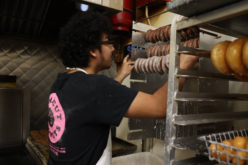 Diego Maldonado hangs freshly glazed cake donuts on a rack at Home Cut Donuts on Jefferson Street, Saturday, March 25, 2023 in Joliet.