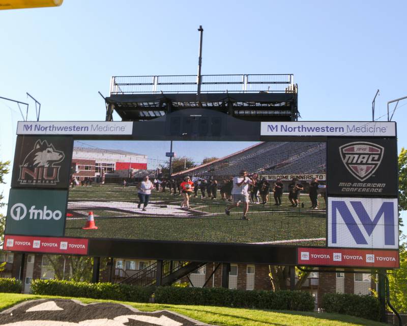 Participants of the Corn Classic run get to see themselves on the Northern Illinois University video board on Sunday Sept. 29, 2024, at Huskie Stadium in DeKalb as the course takes them onto the field .