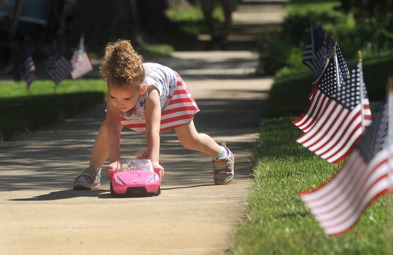 Three-year-old Kennedy West plays with her Barbie car on a flag-lined sidewalk on Main Street before the start of the annual Memorial Day Parade and Service, Monday, May 29, 2023.