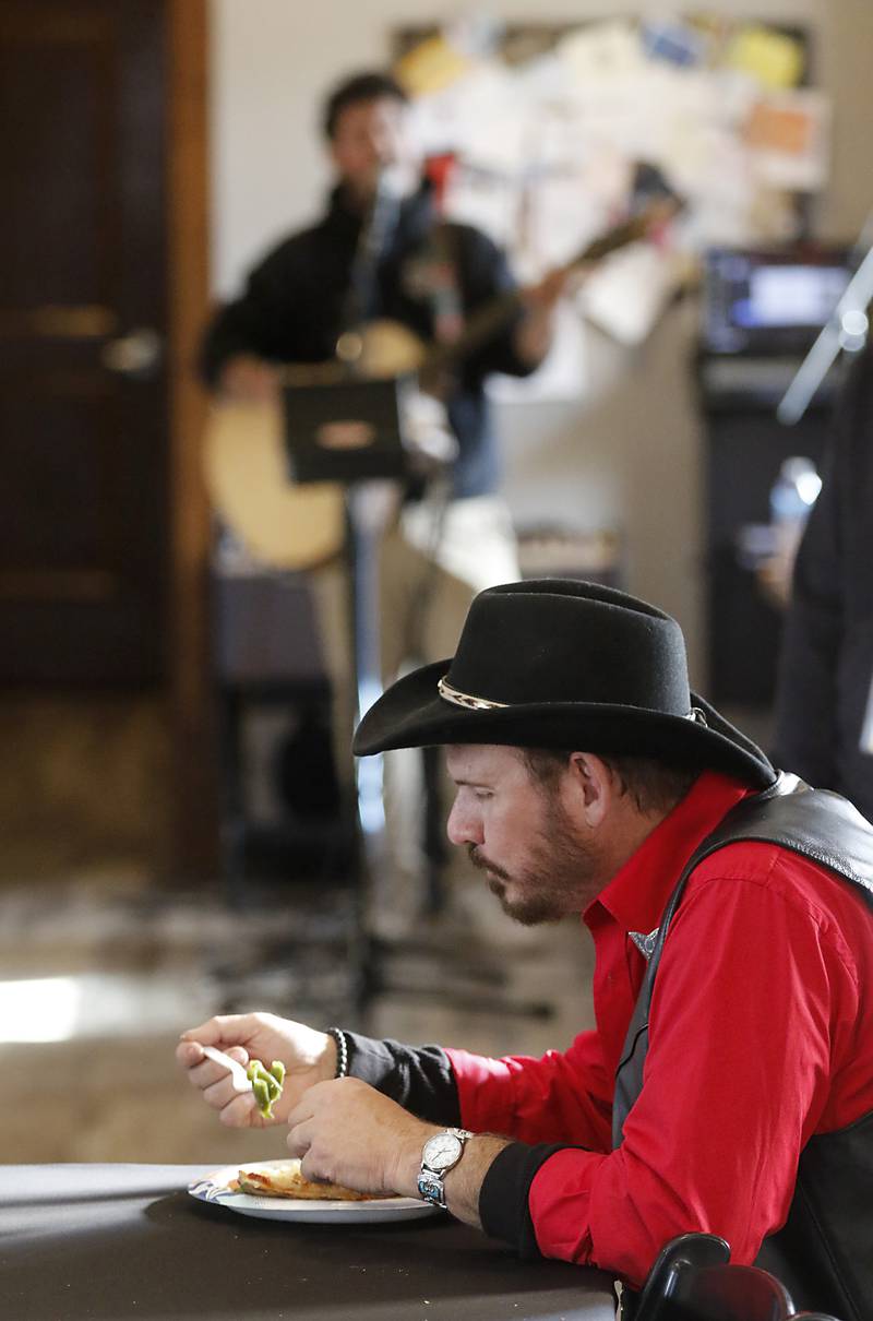 Freddie J. Jr. eats as David “The Jukebox” James performs during a free pre-Thanksgiving luncheon on Wednesday, Nov. 22, 2023, at the Woodstock train depot. This is the second year the meal that was provided through efforts of Warp Corps, MBI Cares, Isabel’s Family Restaurant, and Napoli’s Pizza, all located in Woodstock