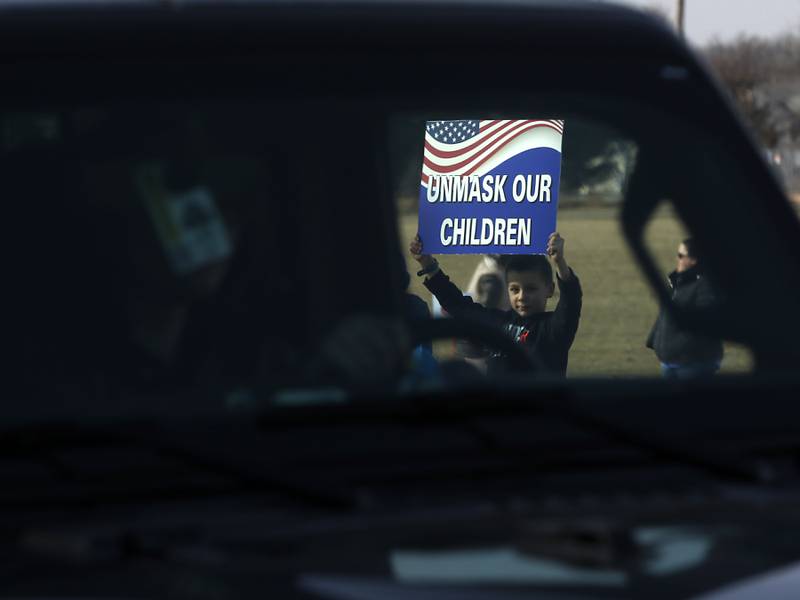 A child holds a sign as a car drives by during a Cary School District 26 anti-mask rally Tuesday, Feb. 15, 2022, along Three Oaks Road at Cary-Grove Park. The event was attend by about 100 people and organized by the Illinois Parents Union Cary.