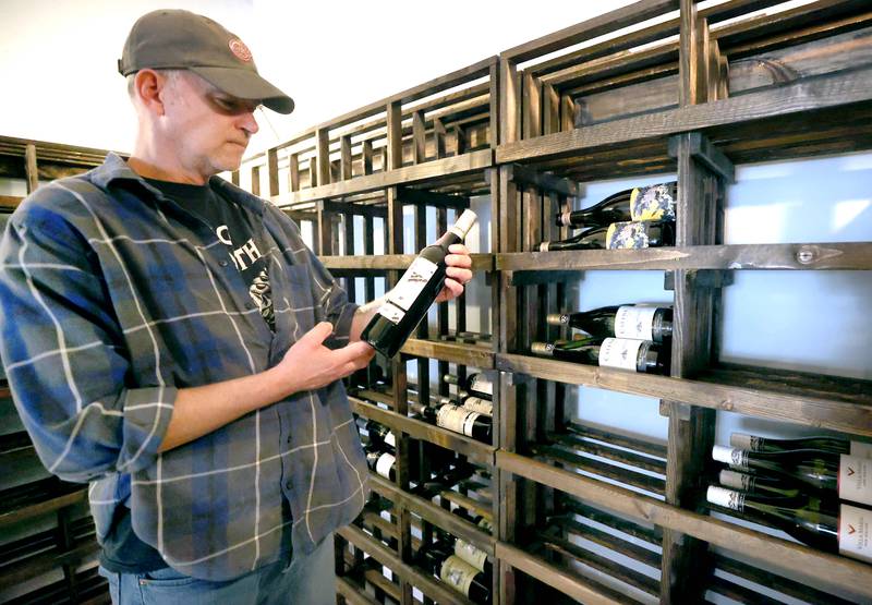 Thomas Sherman, owner of  Class VI Wine & Charcuterie, looks at one of the bottles of wine Friday, April 28, 2023, that will be available at the new restaurant located at 214 E. Lincoln Highway, in DeKalb. Sherman is a U.S. Army veteran.