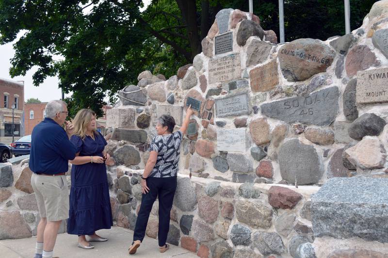 Mt. Morris Economic Development Corporation Executive Director Paula Diehl (right) points to one of many inscriptions on the Veterans Memorial Fountain while speaking with Mt. Morris EDC Chairperson Rob Urish (left) and Kohler Foundation senior manager of art preservation Liesl Testwuide on Thursday, Aug. 29, 2024, in downtown Mt. Morris. The Kohler Foundation, of Kohler, Wisconsin, funded the fountain's restoration at no cost to the village.