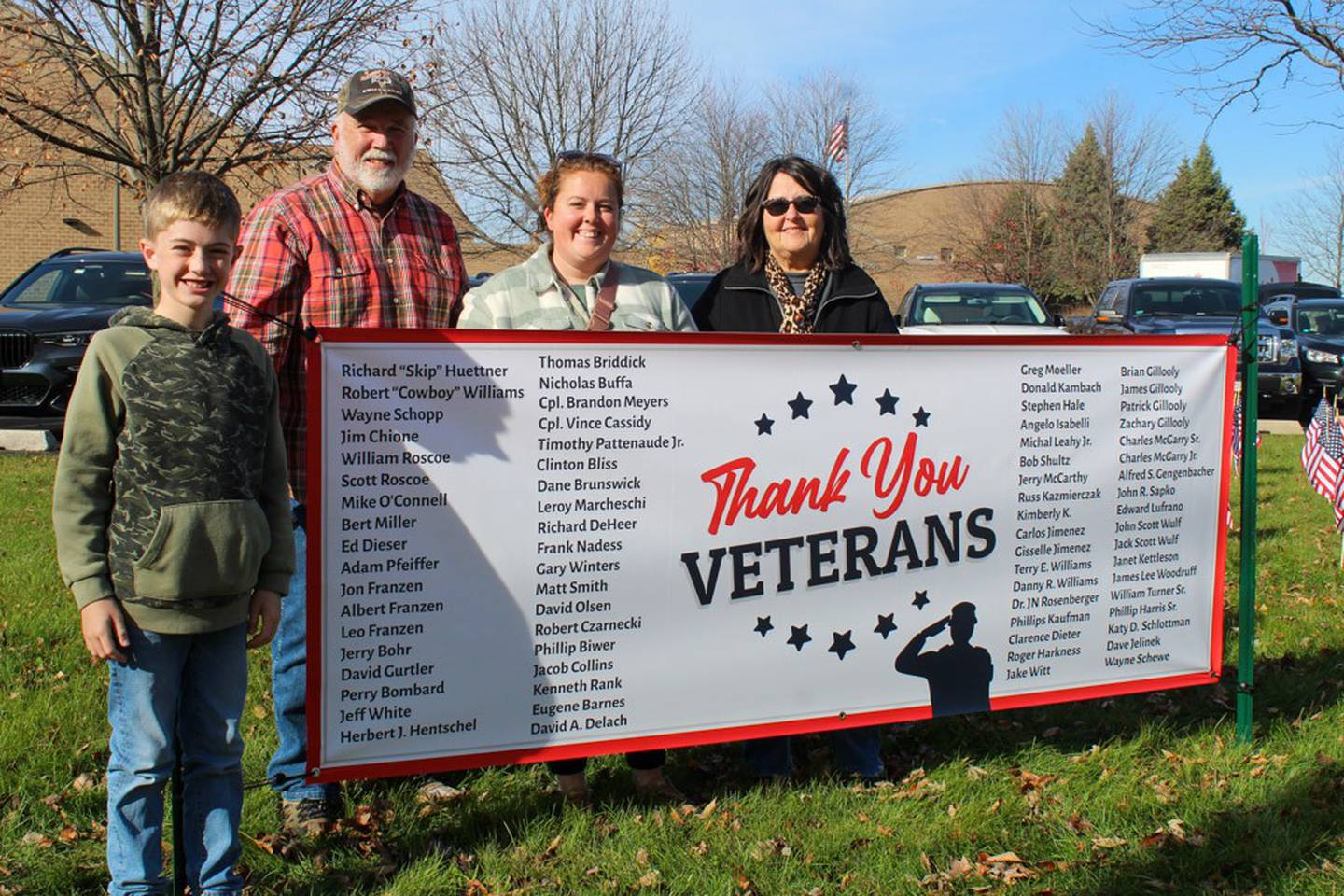 (From left) River View Elementary School fifth-grader Henry Franzen, Mike Murphy, Henry's grandfather, Mallory Franzen, Henry's mom, and Sandy Murphy, Henry's grandmother stand by a sign honoring veterans at the school on Friday, November 8, 2024. Henry raised more than $2,000 to put 192 flags and the sign in front of the school for Veterans Day.