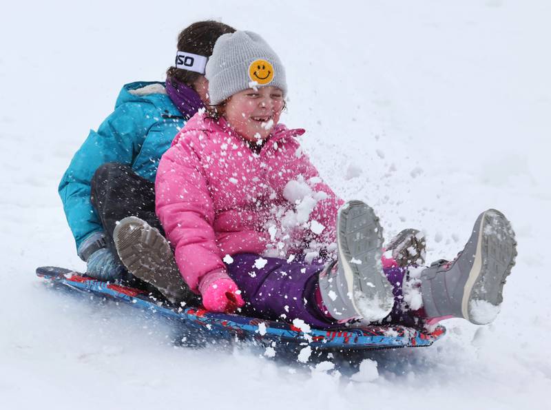 Finley Frankel, (front) 6, and Olivia Weller, 9, both from DeKalb, kick up some snow as the cruise down the sled hill Tuesday, Jan. 9, 2024, at Hopkins Park in DeKalb. Several inches of heavy, wet snow Tuesday was a headache for some and fun for others.