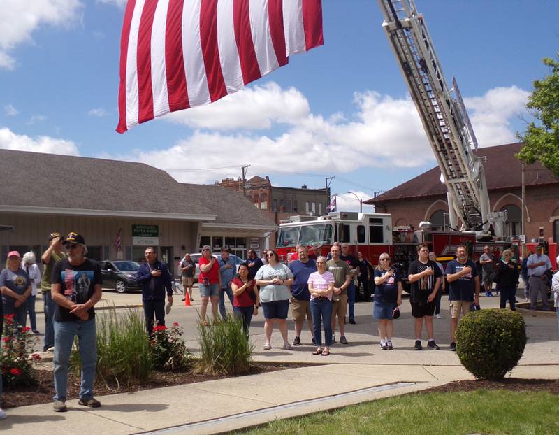 A crowd standing below the large American flag hoisted by a Streator fire engine holds their hands to their heart during "The Star Spangled Banner" at the Memorial Day ceremony at the Veterans Memorial Plaza in Streator's City Park.