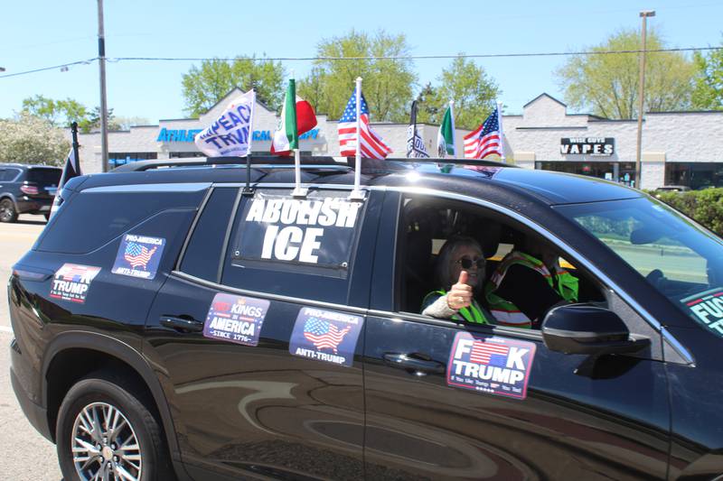 A car drives by protesters lined up along Route 31 in McHenry, donning signs and flags against President Trump and Immigration and Customs Enforcement on April 25, 2026.