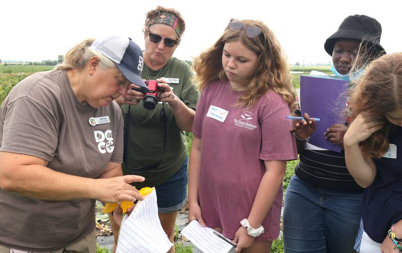 Julie Craig, (left) Walnut Grove Vocational Farm assistant program director, shows DeKalb County Community Gardens Sustainable Food Safari Camp participants some pollinators inside a squash blossom Wednesday, July 27, 2022, during the camp's stop at Walnut Grove Vocational Farm in Kirkland.