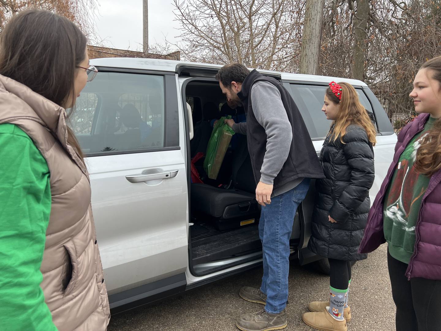 Nick Holtz passes a gift bag to his son,  Benson Holtz in the car on Dec. 24, 2024, as his wife Gina Holtz and two his daughters, Fiona and Calista Holtz wait to climb into – as Gina Holtz called it – the family chariot.