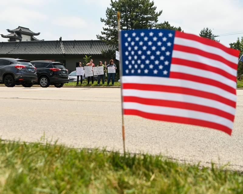 A small American flag flies on the curb as cars pass by while community members hold signs during the No Kings rally on Saturday June 14, 2025, in Lisle near the Tesla dealership.