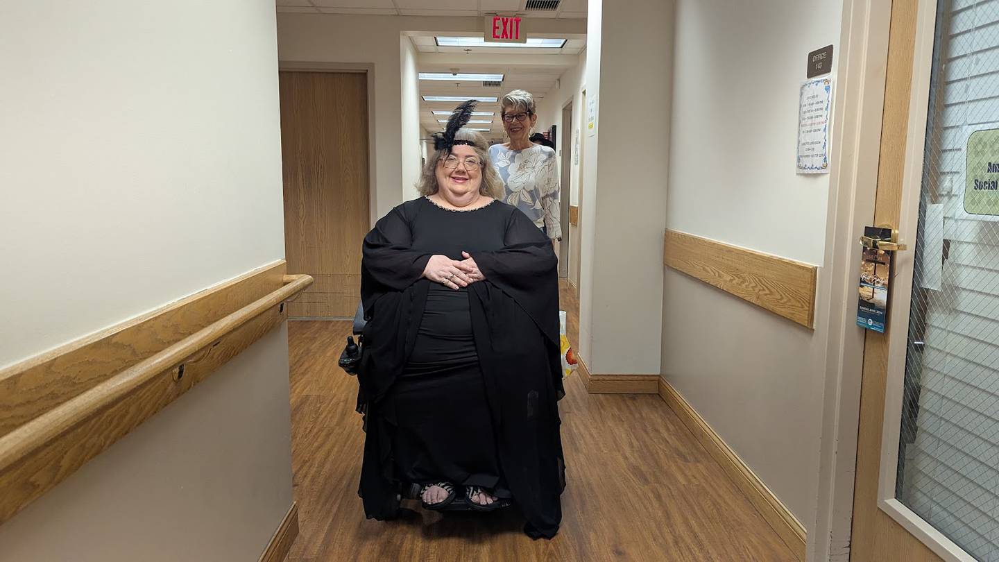 Cookie Ostrem, a resident at Joshua Arms Senior Residences in Joliet and a volunteer for the fashion and talent show, walks behind Karen Cannady, one of the resident models, on Cannady's way to her photo shoot on Friday, April 18, 2025, at Joshua Arms Senior Residences in Joliet.