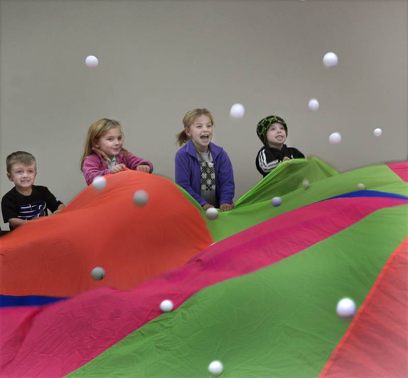 Childen shake a parachute while tossing ping pong balls during a game of Parachute popcorn. This was part of the Parachute Play program Friday at the Reddick Library in Ottawa.