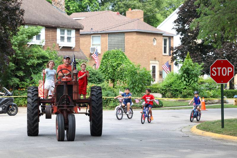 Jeff Grosso, of Kankakee, drives a tractor with his kids Genevieve, 13, left, and Josef, 8, as they pace the first lap of the Kids' Bike Ride during the Riverview Historic District's annual 4th of July Celebration on Friday, July 4, 2025.