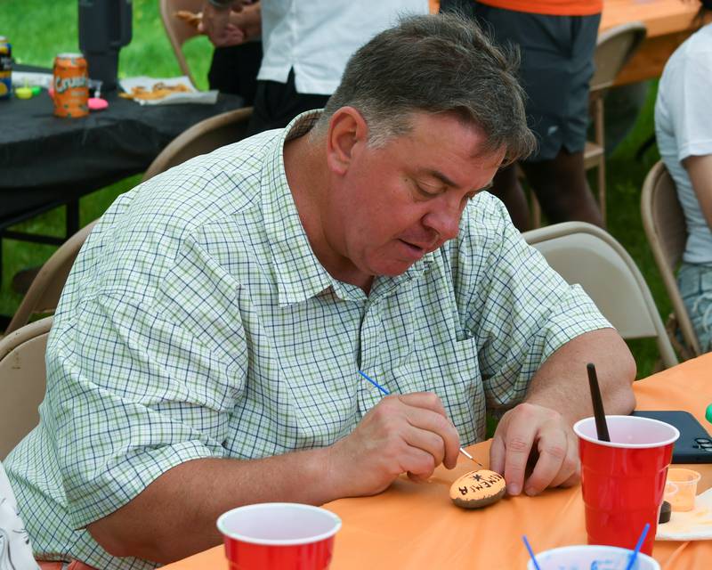 Richard Collins, of Malta, educator coworker of Andrea Elion, paints a rock on Saturday, June 7, 2025, during the Ezra Hill Jr. Memorial Foundation’s 5th annual rock painting event held at Tyler Elementary School in DeKalb. The foundation was created by Andrea to memorialize her late son, who was shot and killed in 2019.