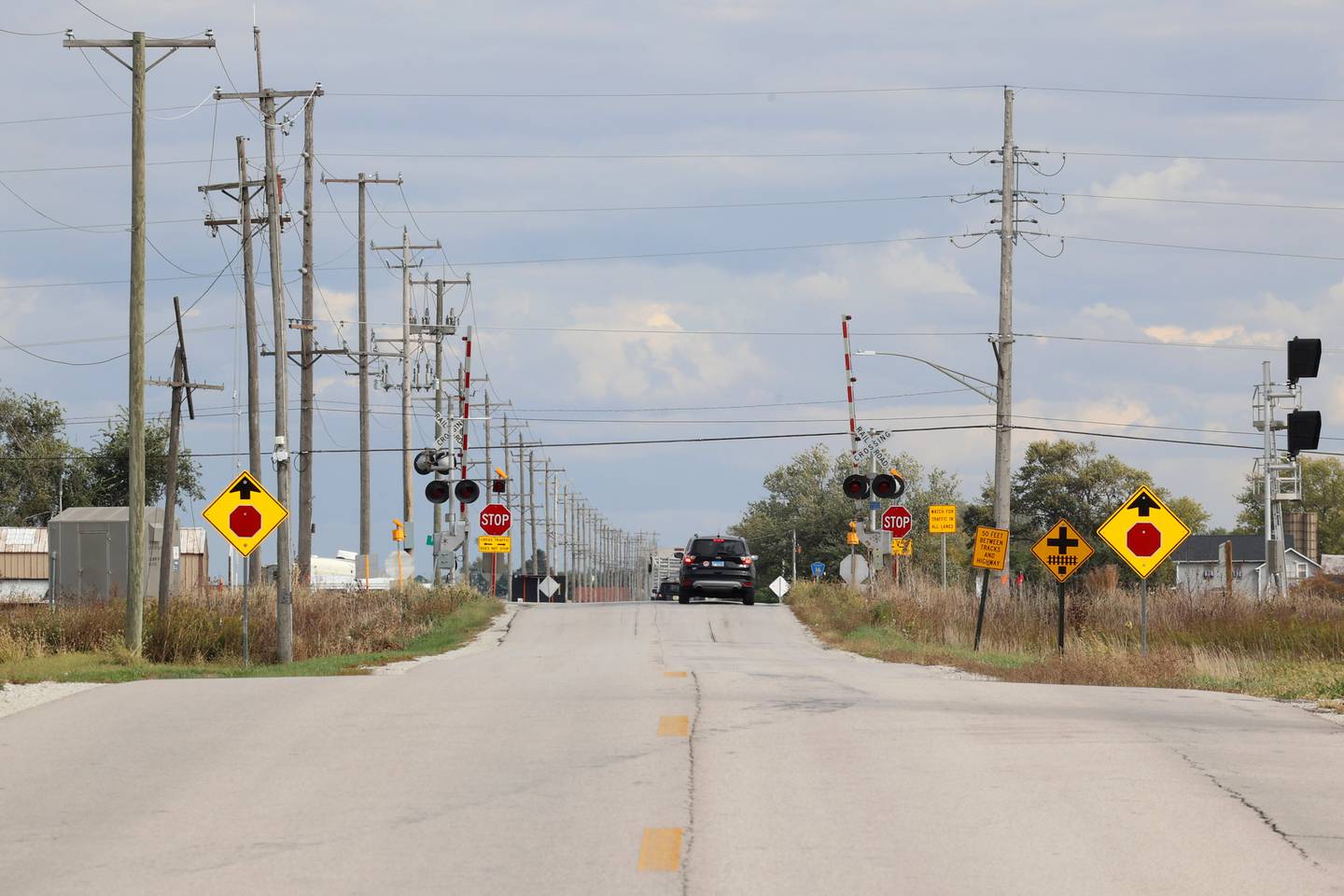 A number of signs warn drivers of the stop sign, railroad tracks and stopping distance looking east on County Line Road as a hill obscures the intersection at IL Route 50 on Tuesday, Oct. 21, 2025. 
Crews were at work that day preparing for a traffic pattern change, creating a four-way stop, at the accident-prone intersection where 18 accidents and four fatalities have occurred this year.
