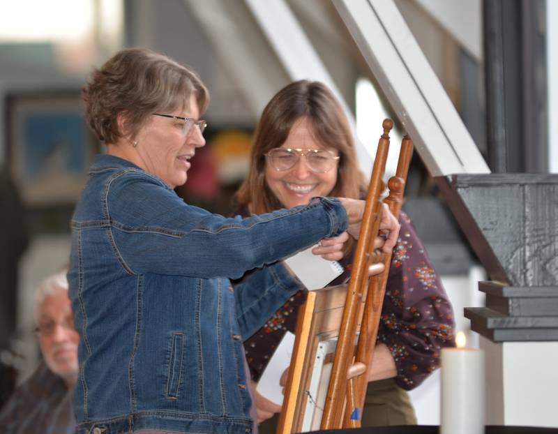 Molly McNett smiles as her art work is secured with her number with the help of a Serenity Home & Hospice volunteer during Art Dash on Wednesday, April 10, 2024 at River's Edge Experience in Oregon.