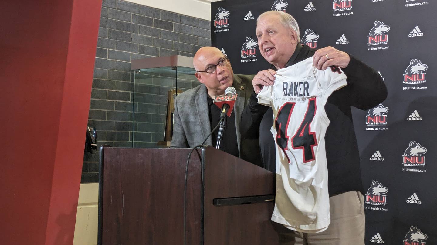 NIU athletic director Sean Frazier (left) presents Bill Baker, play-by-play broadcaster for Huskies athletics, with a jersey at media day on Tuesday, August 15, 2023. The school announced this season, Baker's 44th, will be his last.
