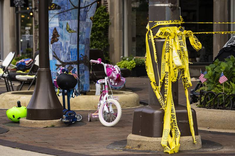 Crime scene tape hangs from a pole near a child's bicycle as members of the FBI's Evidence Response Team Unit investigate near Central Avenue and Green Bay Road in downtown Highland Park, Ill., on Tuesday, July 5, 2022,  one day after a gunman killed several people and wounded dozens more by firing an AR-15-style rifle from a rooftop onto a crowd attending a Fourth of July parade. (Ashlee Rezin/Chicago Sun-Times via AP)