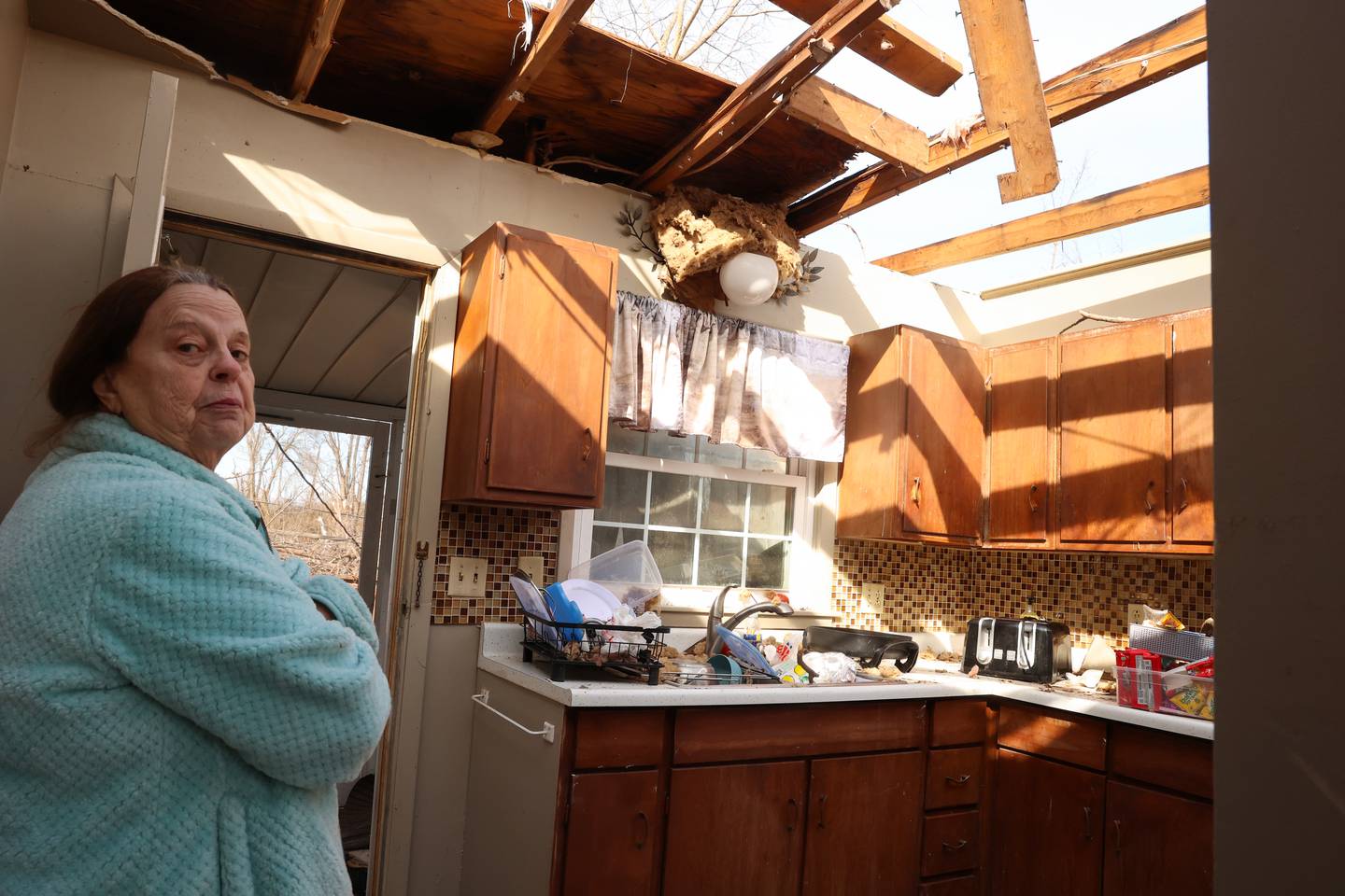 Aroma Park resident Patricia Kime recounts the damage to the kitchen of her home on Strasma North Drive, which was destroyed by the March 10 EF-3 tornado. The bathroom she took shelter in was the only intact room in the house, she said.