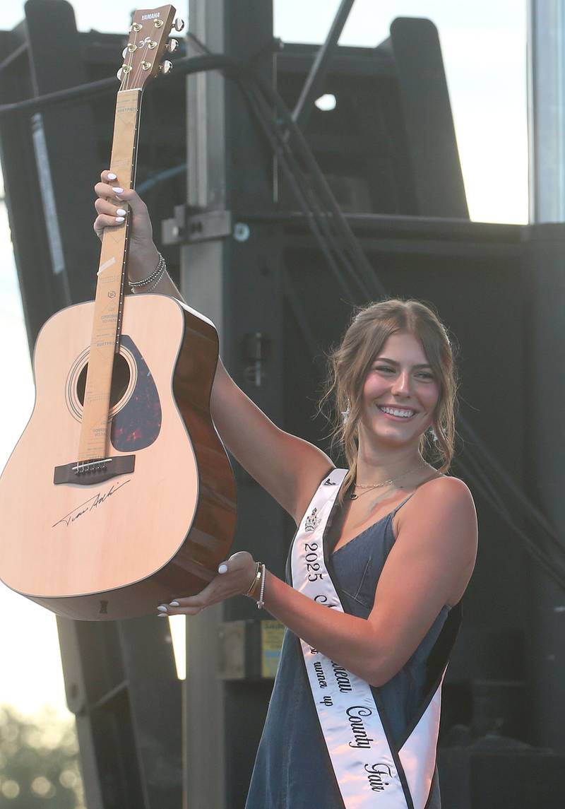 Matilda Mitchell, Bureau County Fair Miss, 1st Runner-Up, holds an autographed guitar during a live auction on-stage before the Trace Adkins concert on Thursday, Aug. 21, 2025 at the Bureau County Fair in Princeton.