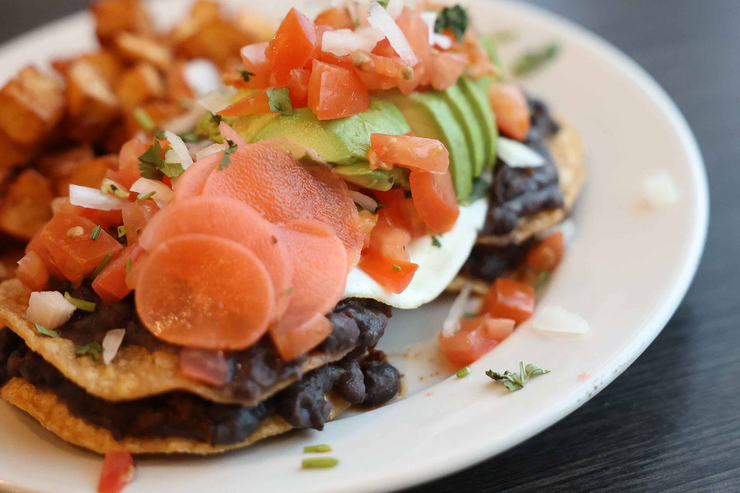 A plate of the Huevo Rancheros, two tostadas topped with black beans, egg, avocado, tomato, onion, cilantro and pickled radish served with ranchero sauce, sits on the table at Jitterhead on Wednesday, Dec. 11, 2024 in Crest Hill.