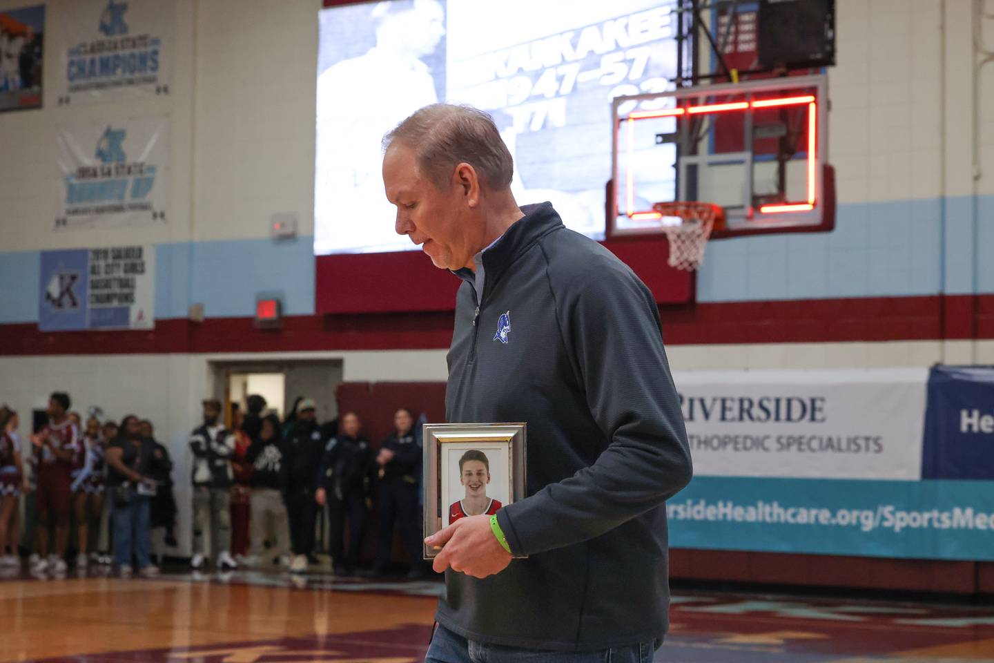 Scott Hollywood enters the gym carrying a photo of his late son, Zach Hollywood, who was honored as part of the All-75th Anniversary Team on the opening night of the 75th Kankakee Holiday Tournament on Friday, Dec. 26, 2025