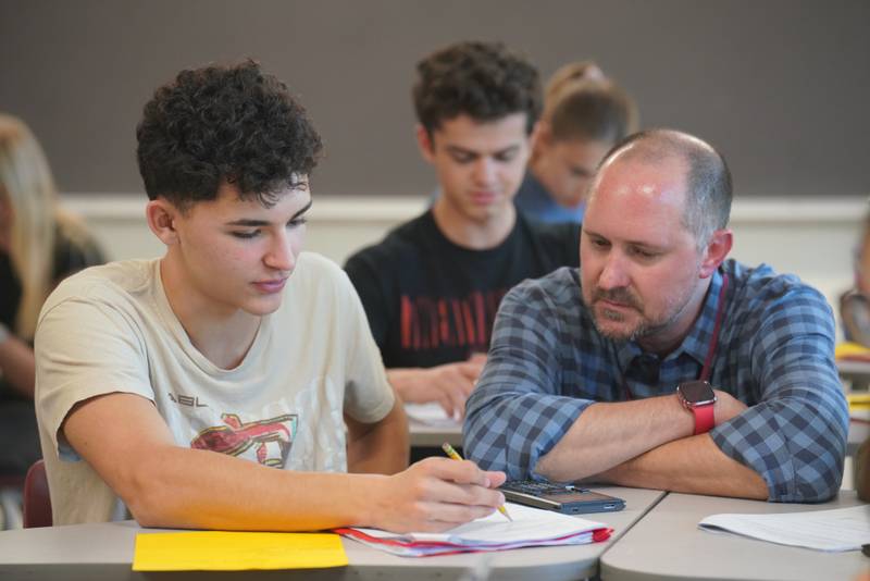 Jack Instefjord, left, a Prairie Ridge High School senior, verifies his answer on a dual credit statistics worksheet with teacher Erik Zier, right, on Tuesday, Oct. 29, 2024. Students earning advanced course credits like these are showing higher graduation rates across the state.