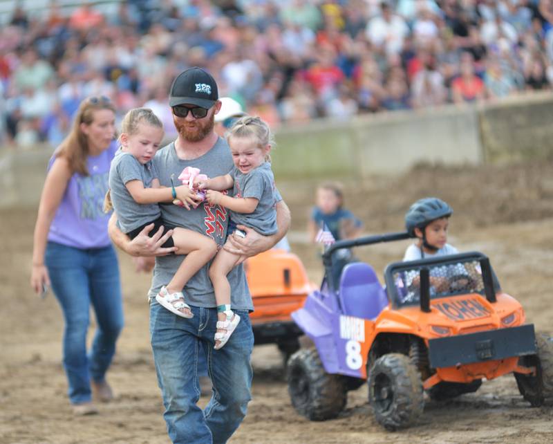 Kyle Hahn of Erie carries his two daughters, Emery, 2, and Easley, 4, after they competed in the kids event at the Whiteside County Fair's demolition derby on Saturday, Aug. 17, 2024.