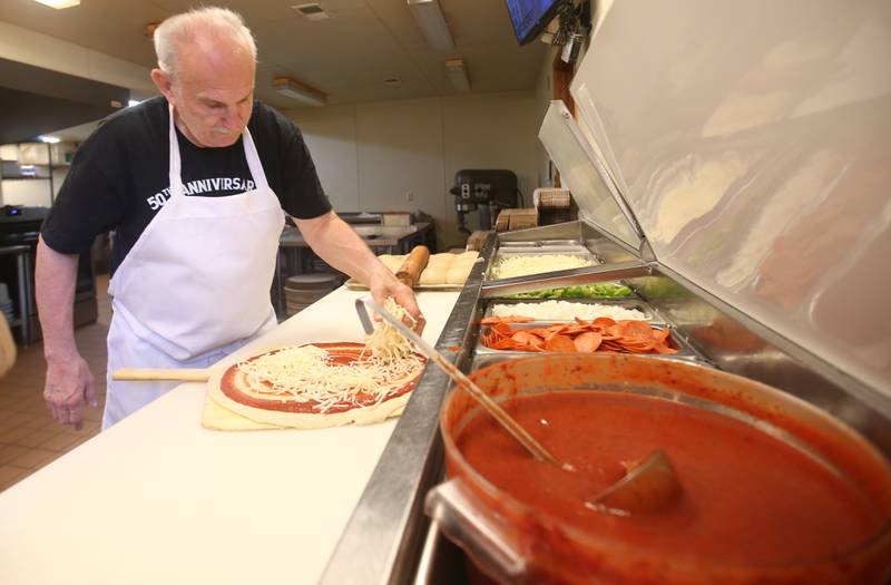 Joe Evola, owner of Sam's Pizza, places cheese on a pizza on Wednesday, June 4, 2025, at his pizza restaurant in Marseilles.  Sam's Pizza celebrates its 50th anniversary in business this year.