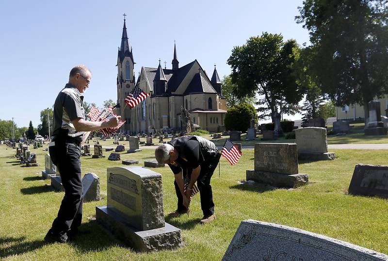 U.S. Army veteran Alex Januk holds flags as volunteer Bruce Preston places a flag at a grave on Friday, May 26, 2023, in St. John the Baptist Cemetery, in Johnsburg.