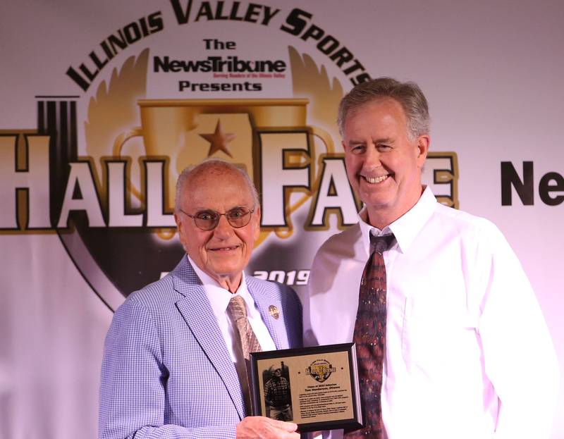 Lanny Slevin Emcee, presents an award to Tom Henderson Jr. as he accepts the award of his father Tom henderson Sr. during the Shaw Media Illinois Valley Sports Hall of Fame on Thursday, June 8, 2023 at the Auditorium Ballroom in La Salle. Henderson was the boys and girls tennis coach at Ottawa Township High School from 1958-2007.