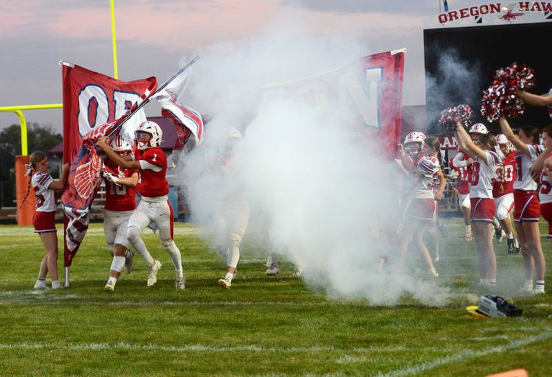 Seniors Benny Olalde (1) and Keaton Salsbury (10) lead the Oregon Hawks through their banner at the start of their Homecoming game with Rock Falls on Friday, Sept. 19, 2025 at Landers-Loomis Field in Oregon.