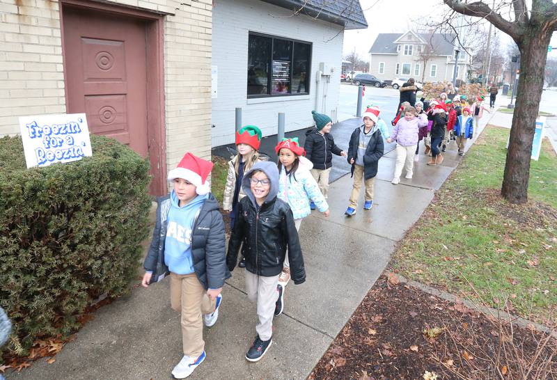 Marquette Academy Grade School first grade students walk into the WCMY radio station to sing Christmas carols during the Freezin' for a Reezin' on Friday, Dec. 1, 2023 in Ottawa. Donations from the event benefited the Ottawa Community Basket.